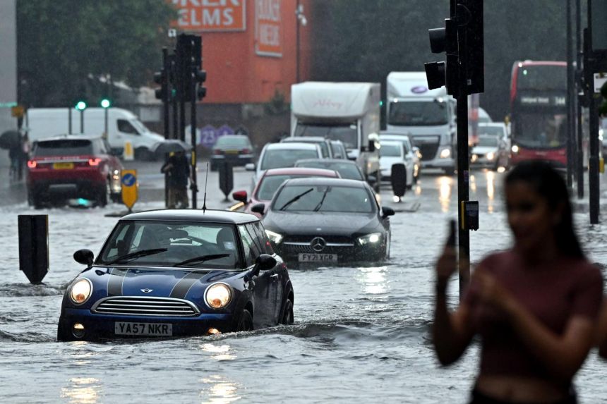 Cars drive through deep water on a flooded road in London, on July 25, 2021.