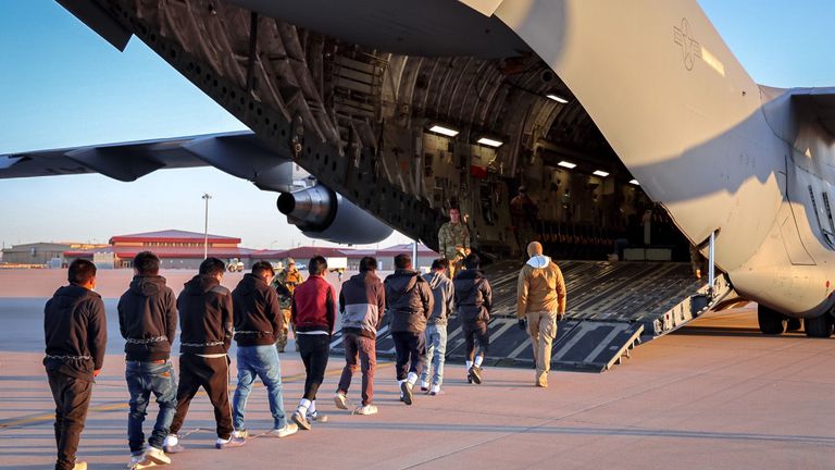 Men in shackles being led on to a military plane. Pic: X/PressSec